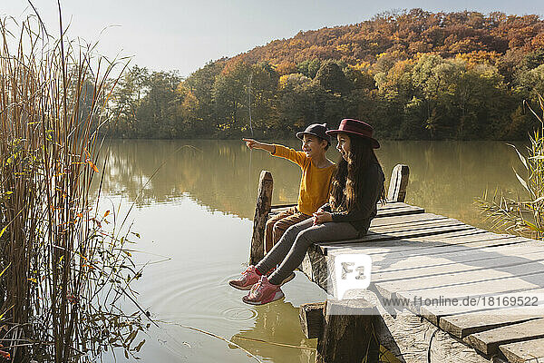 Boy pointing to girl sitting together on jetty at lake