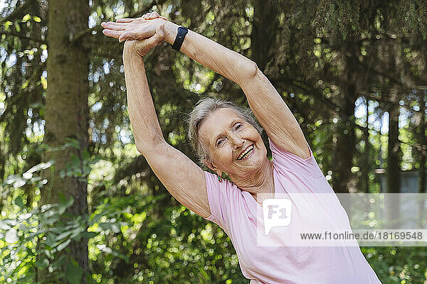 Happy senior woman with arms raised practicing stretching exercise at park