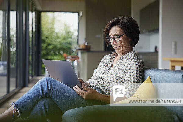 Frau sitzt zu Hause auf dem Sofa und benutzt Laptop