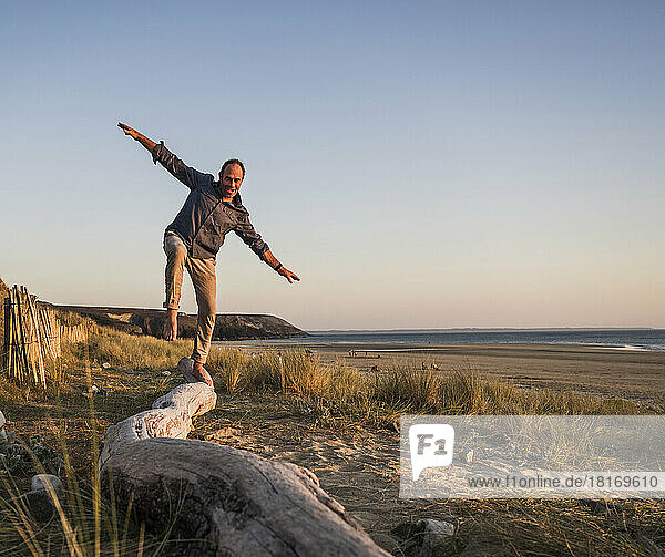 Playful man with arms outstretched balancing on log