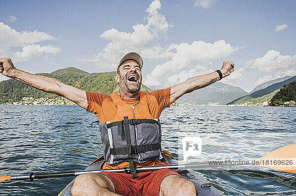 Aufgeregter reifer Mann schreit mit ausgestreckten Armen auf dem See