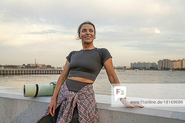 Smiling mature woman with exercise mat leaning on wall
