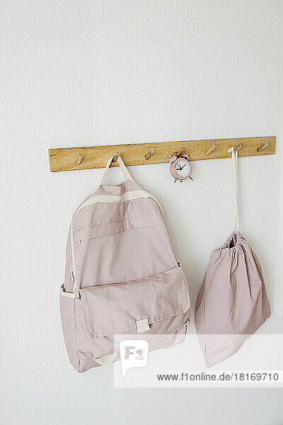 Pink color backpacks and alarm clock hanging on wall hook