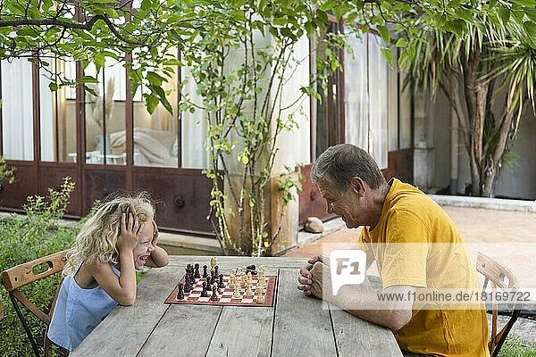 Enkelin und Großvater spielen Schach im Garten