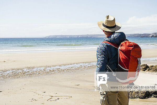 Mann mit Rucksack bewundert das Meer am Strand