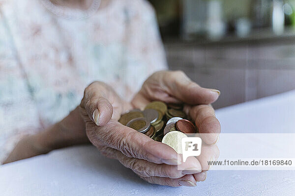 Senior woman holding coins over table at home