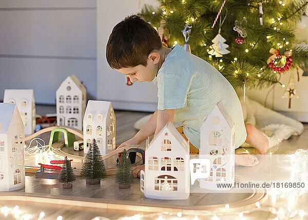 Junge spielt mit Spielzeugeisenbahn in der Nähe des Weihnachtsbaums zu Hause