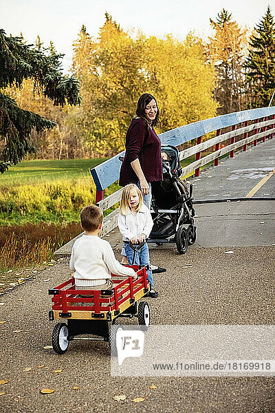 Eine Mutter und ihre kleinen Kinder überqueren eine Brücke über einen Fluss in einem Stadtpark während der Herbstsaison; ihre kleine Tochter hat das Down-Syndrom; St  Albert  Alberta  Kanada