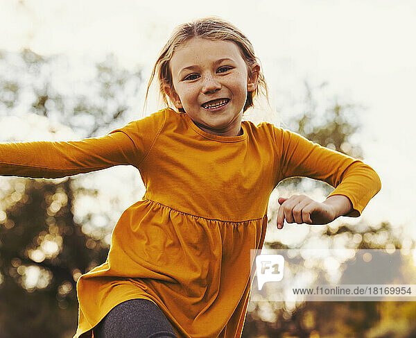 Junges Mädchen  das an einem warmen Herbsttag in einem Stadtpark über das Gras rennt und in die Luft springt; St. Albert  Alberta  Kanada
