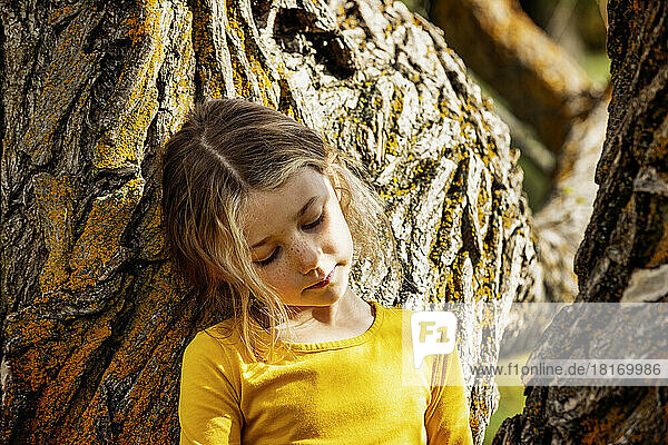 Young girl playing near a tree and pausing for a moment in a city park on a warm fall afternoon; St. Albert  Alberta  Canada
