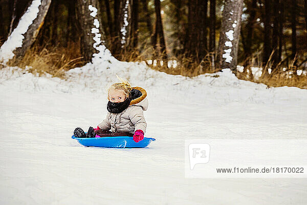 Young Girl With Blond Hair Riding A Blue Plastic Sled Down A Snowy Hill At A Mountain Resort; Fairmont Hot Springs  British Columbia  Canada