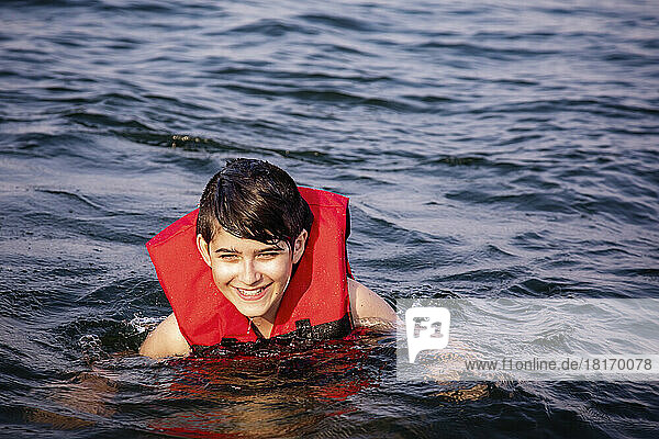 Young boy floating and swimming in a lake with a lifejacket  Lac Ste. Anne; Alberta Beach  Alberta  Canada