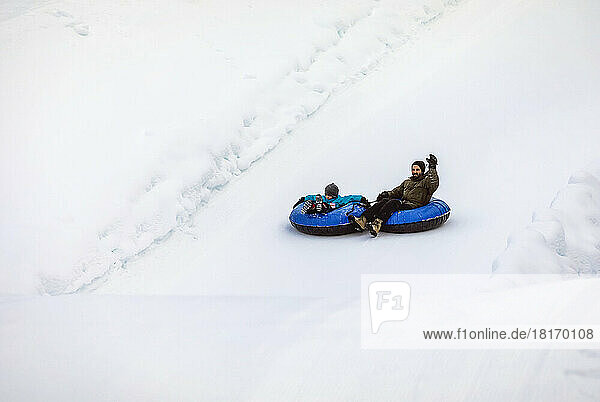 Father and son tubing down a ski hill; Fairmont Hot Springs  British Columbia  Canada