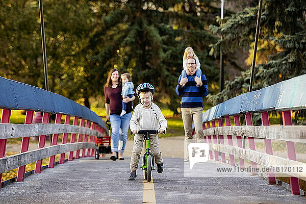 Young family crossing a bridge over a river in a city park during the fall season and their baby daughter has Down Syndrome; St. Albert  Alberta  Canada