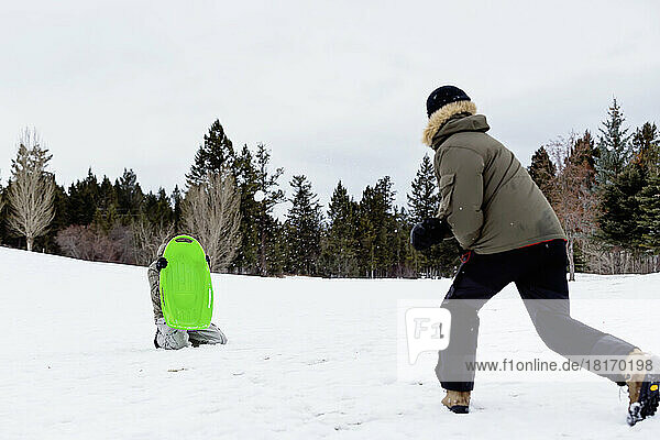 A Man Throws Snowballs At Another Adult Who Is Holding A Sled To Block Them At A Mountain Resort; Fairmont Hot Springs  British Columbia  Canada
