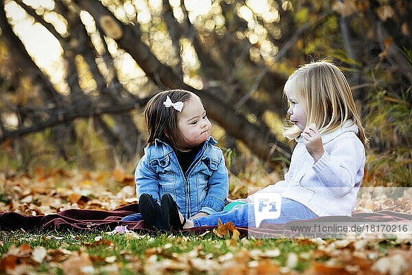 Zwei junge Schwestern  eine mit Down-Syndrom  spielen zusammen in einem Stadtpark während der Herbstsaison; St. Albert  Alberta  Kanada