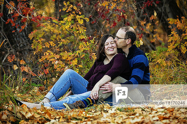 Porträt eines reifen Ehepaars  das während der Herbstsaison in einem Stadtpark Zeit miteinander verbringt  wobei der Ehemann seine Frau küsst; St. Albert  Alberta  Kanada