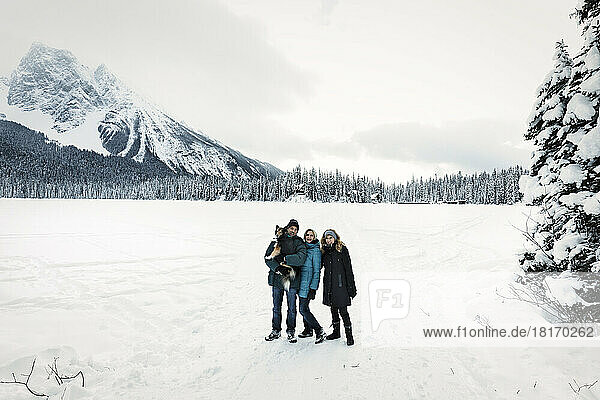 Tourists with a dog pose for the camera while hiking across a frozen Emerald Lake with the Rocky Mountains in the background during winter in Yoho National Park; British Columbia  Canada