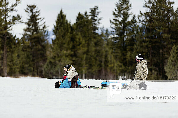 Ein Vater beobachtet zwei kleine Kinder  die beim Schlittenfahren im Schnee spielen; Fairmont Hot Springs  British Columbia  Kanada