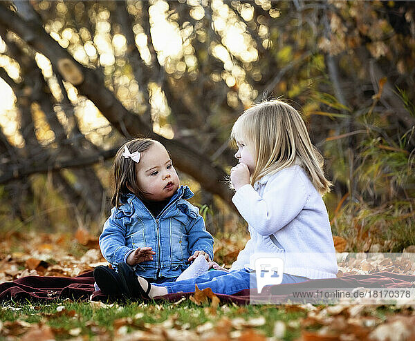 Two young sisters  one with Down Syndrome  playing together in a city park during the fall season; St. Albert  Alberta  Canada