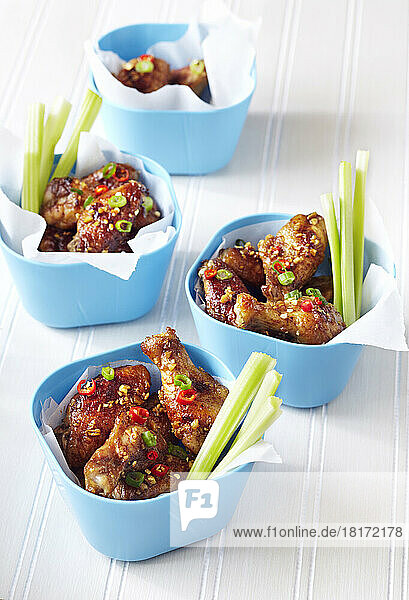 Chicken wings covered in chili and scallion sauce in blue bowls with celery sticks