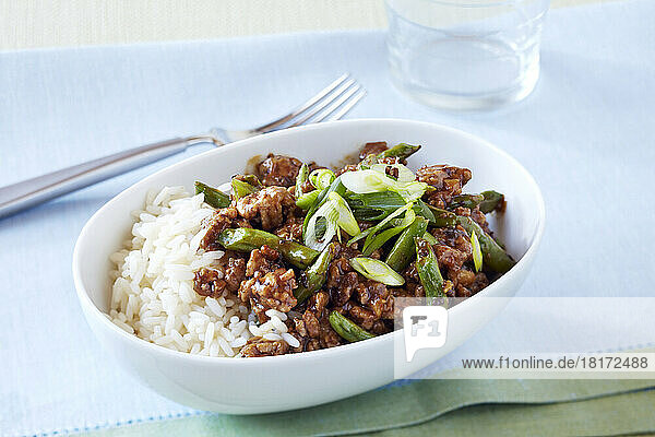 Pork  asparagus and green onion stir fry with white rice in a bowl