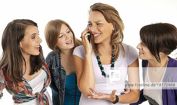 Four  young women laughing and looking at each other  one young woman using cell phone  studio shot on white background