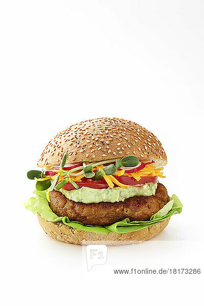 A chickpea burger on a sesame bun with lettuce  chickpeas  guacamole  shredded cheddar cheese  tomatoes  radish  and sprouts close-cut on a white background