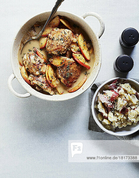 Apple braised chicken thighs in baking dish with side dish of smashed potatoes