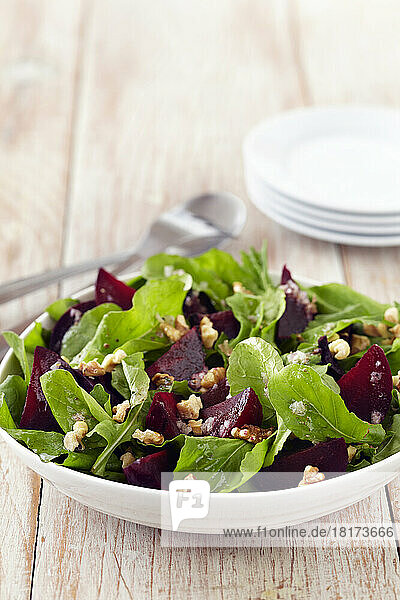 Beet salad with baby greens and walnuts in a bowl with serving utensils and side plates
