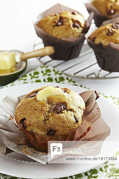Chocolate chip muffins with butter on top and a cooling rack in the background
