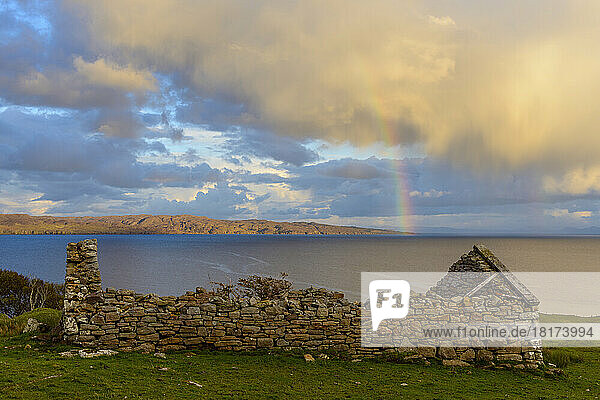 Remains of a stone house on the Isle of Skye with a rainbow appearing over the coast in Scotland  United Kingdom