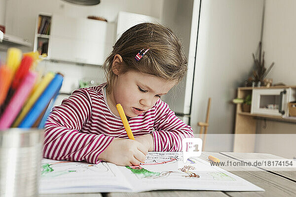 Girl Sitting at Table and Colouring Pictures