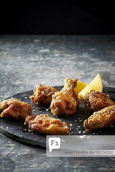 Breaded and salted chicken wings with lemon wedges on a slate platter