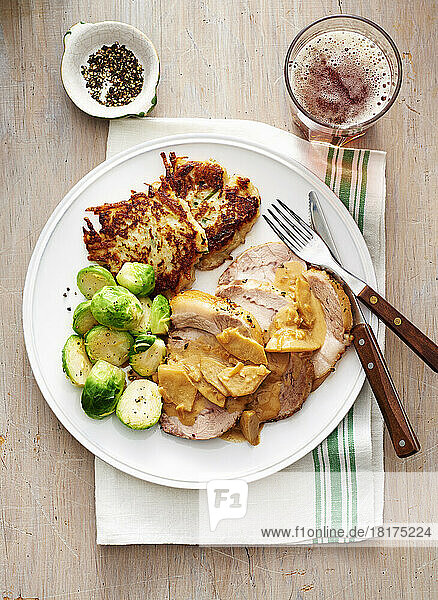 Roast pork with apple sauce  brussels sprouts and potato patties on a white plate with fork and knife