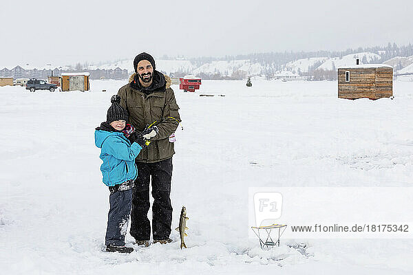 Father and his young son catch a fish while ice fishing on frozen Windermere Lake  Windermere Lake Provincial Park; Invermere  British Columbia  Canada