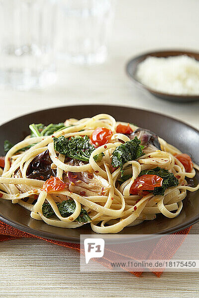 Linguine pasta with tomato  leafy greens and crushed red pepper on dark brown plate