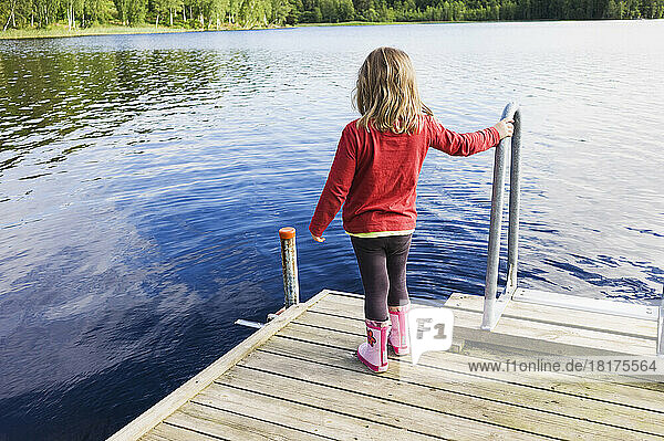 3 year old girl in red shirt on wooden dock looking at a lake  Sweden