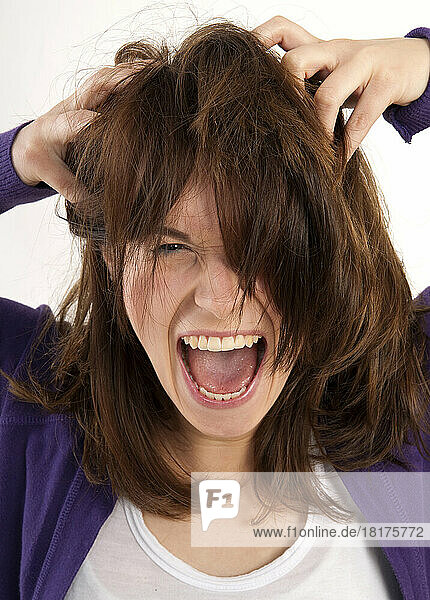 Close-up portrait of young  brown-haired woman screaming and looking at camera with hands in her hair  studio shot on white background