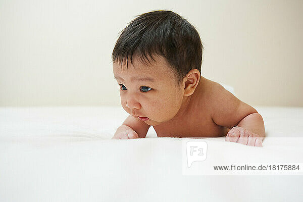 Newborn Asian baby with baby acne lying on stomach  studio shot on white background