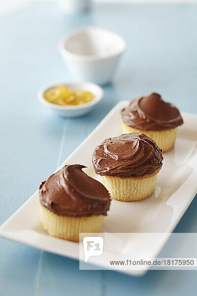 Chocolate frosted cupcakes on a blue background with small bowl of lemon zest in the background