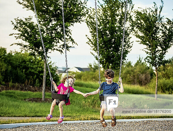Young girl and boy holding hands while playing on a swing set at a playground; St. Albert  Alberta  Canada