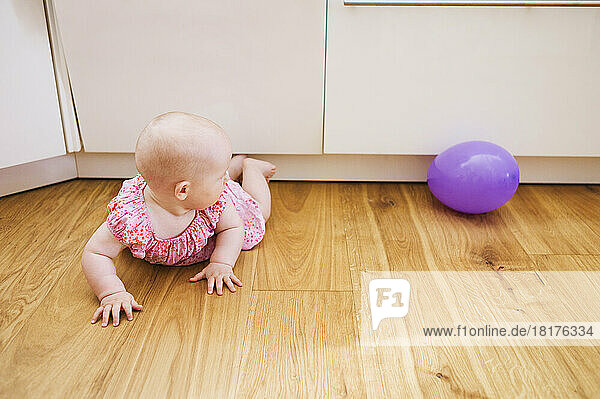 Baby Girl lying on floor and Looking at Purple Balloon
