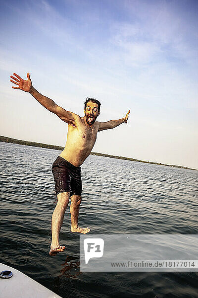 Man jumping from a boat into the lake with a happy expression on his face  Lac Ste. Anne; Alberta Beach  Alberta  Canada