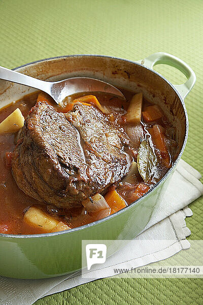 Beef pot roast with root vegetables in an enamel cast iron pot on a green background