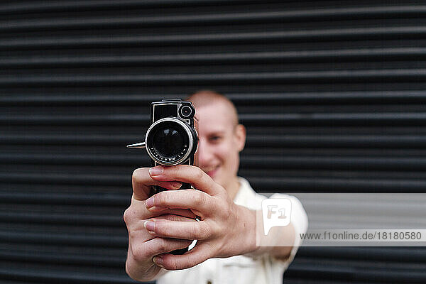 Non-binary person holding video camera in front of shutter