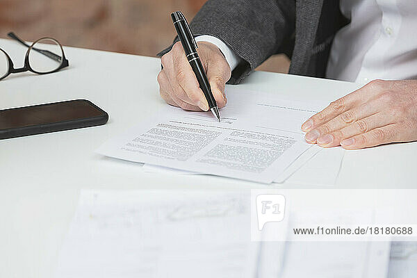 Hand eines Geschäftsmannes  der am Schreibtisch einen Vertrag mit einem Stift unterzeichnet