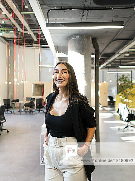 Happy businesswoman standing with hands in pockets at office