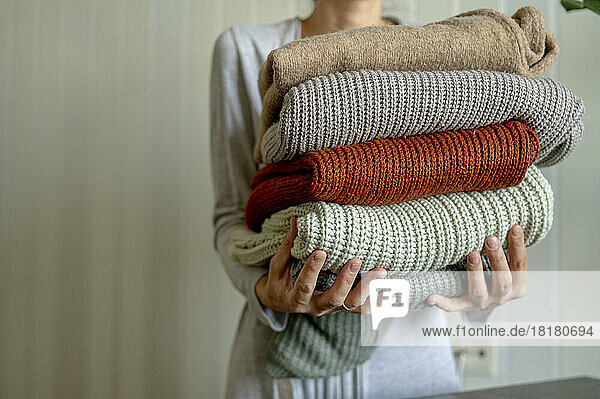 Woman holding multi colored sweaters at home