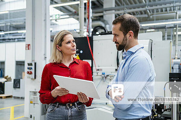Businesswoman holding tablet PC looking at colleague in factory